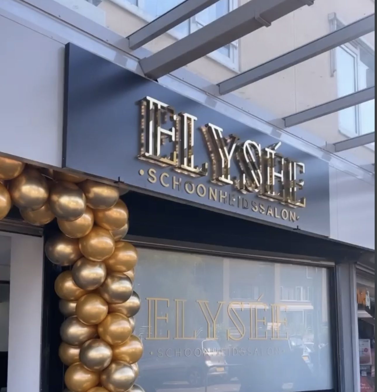 De gevel van Elysée: gouden letters Elysée Schoonheidssalon boven het raam, met een boog van gouden ballonnen