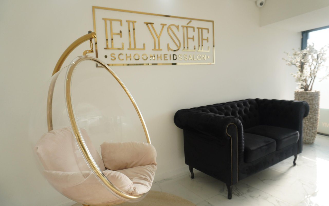 De lounge van Elysée: het gouden Elysée-logo aan de muur, een gouden hangstoel en een zwarte chesterfield op witte marmervloer